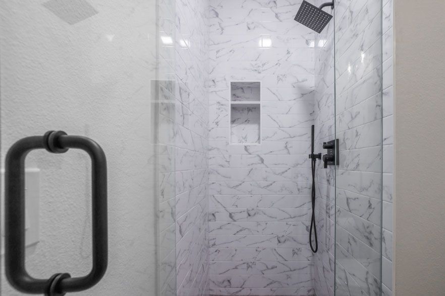 Modern marble-tiled shower with black grab bar and handheld showerhead
