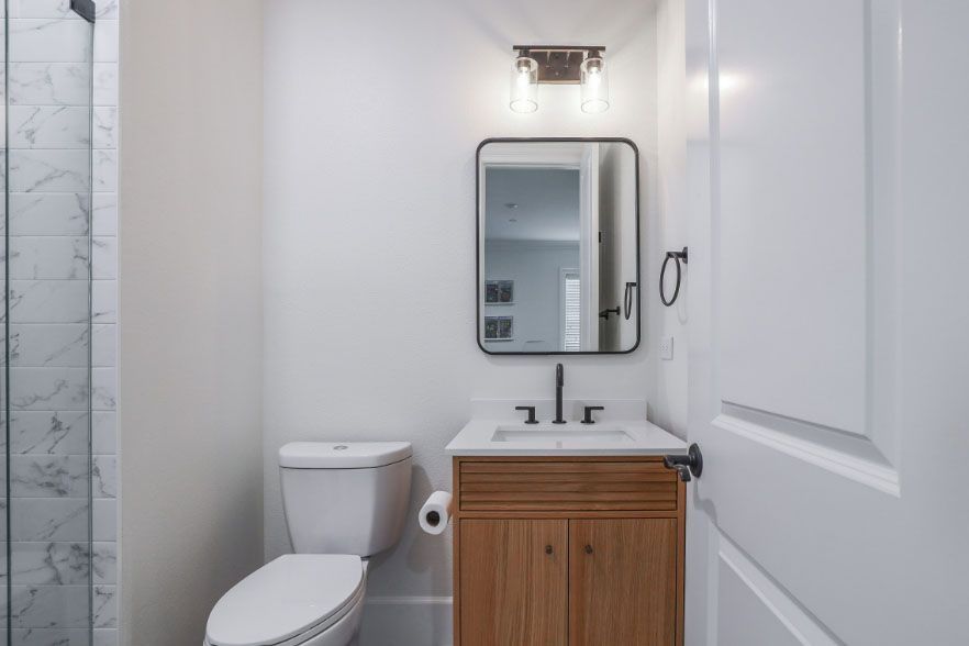Small white bathroom with toilet, vanity sink, mirror, and wall light.