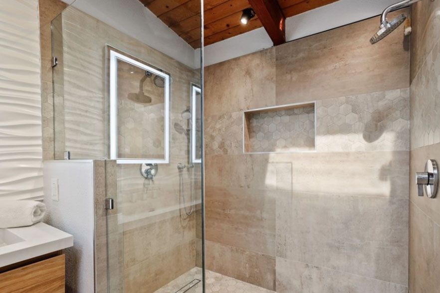 Modern walk-in shower with beige tile, glass door, bench, and built-in niches