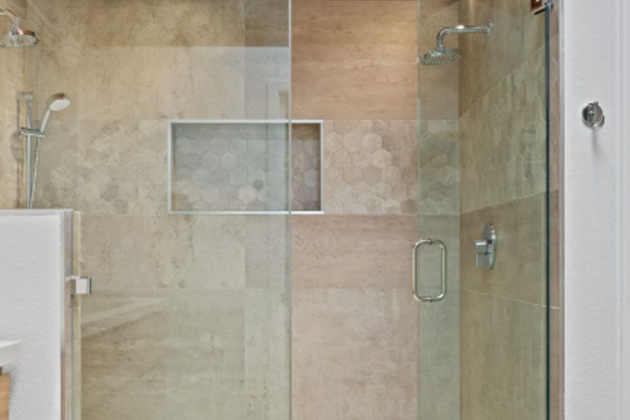 Glass shower enclosure with beige tiled wall and recessed shelf in a bathroom