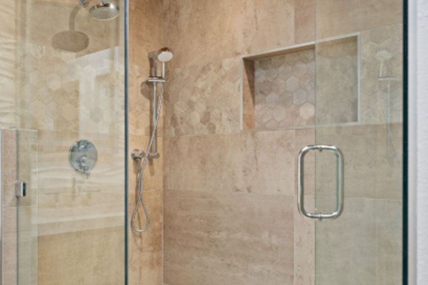Glass shower enclosure with beige tile and built-in shelf in a modern bathroom