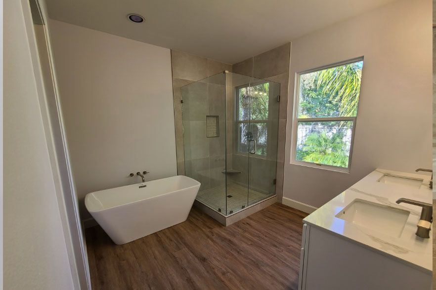 Modern bathroom with a freestanding tub, glass shower, vanity, and wood-look flooring.
