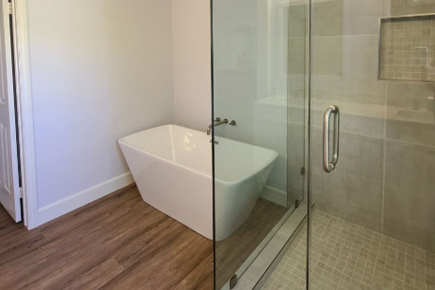 Modern bathroom with a freestanding tub beside a glass-enclosed shower and wood-look floor