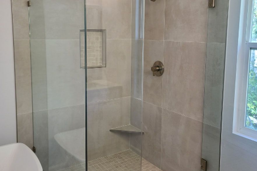 Glass walk-in shower with beige tile, mosaic floor, built-in shelf, and window light