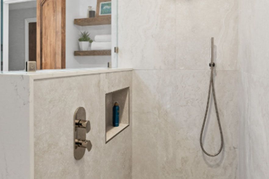 Modern bathroom shower with marble walls, built-in shelf, and handheld showerhead
