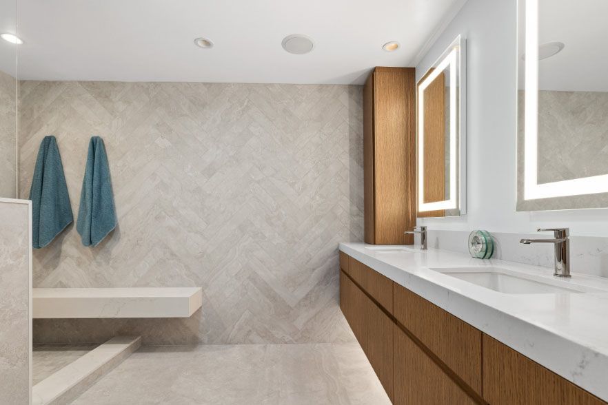 Modern bathroom with wood vanity, large mirror, white sink, stone wall, bench, and teal towels