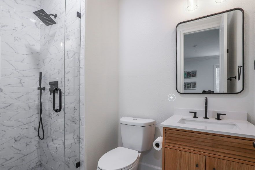 Modern bathroom with marble shower, toilet, vanity, and black-framed mirror