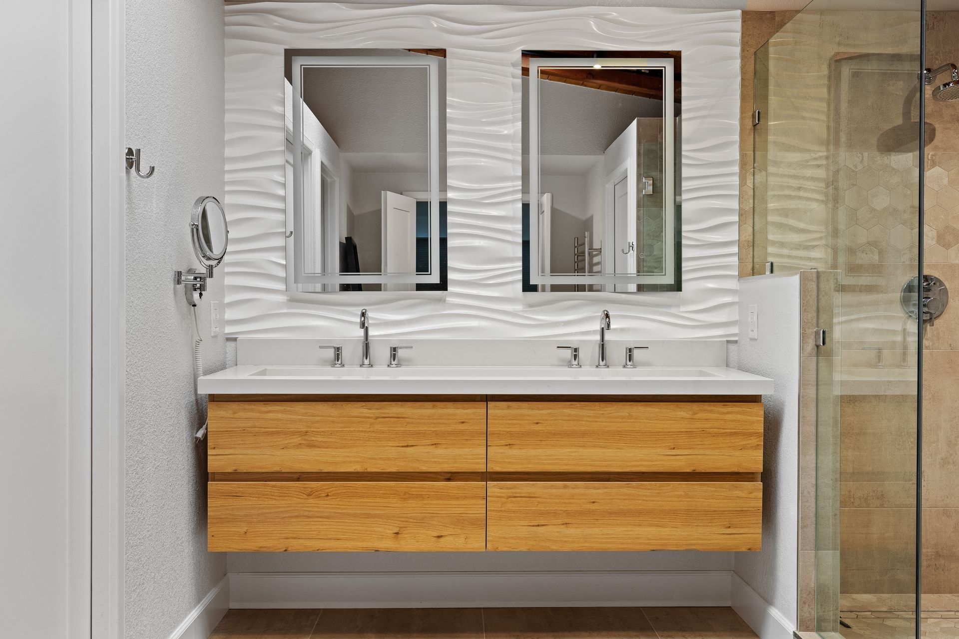 A modern bathroom vanity with dual rectangular mirrors, white wavy tile wall, and light wood floating cabinets.