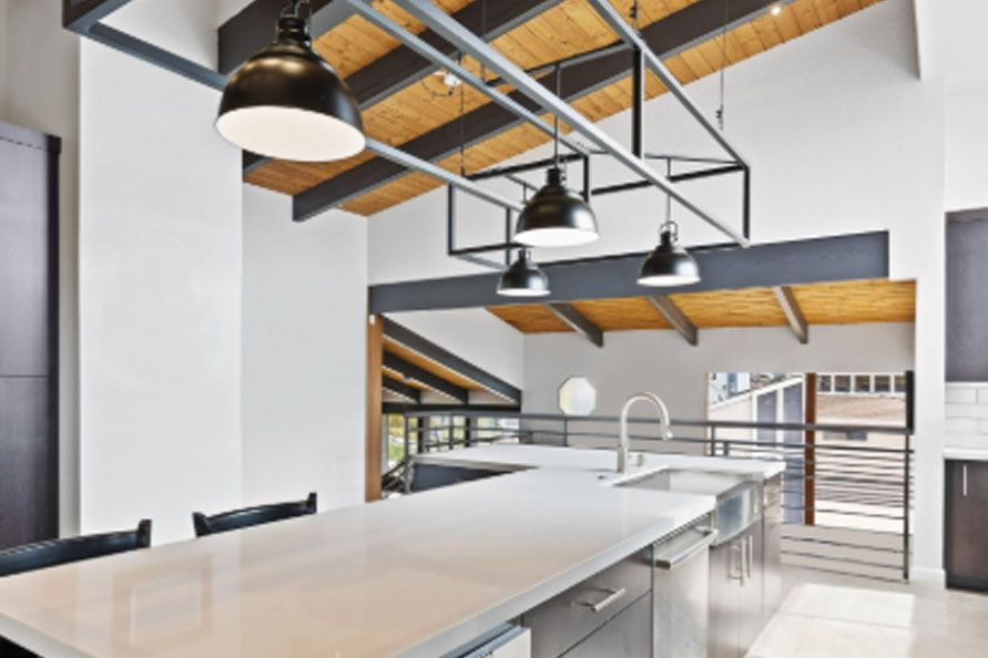 Modern open-plan kitchen with white island, black pendant lights, and exposed wood ceiling beams