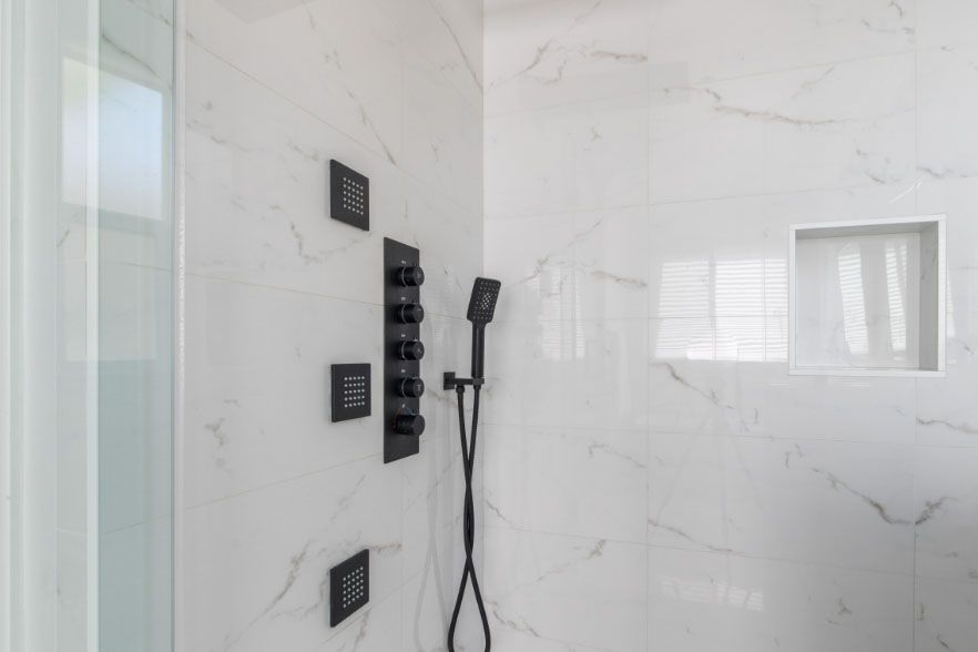 Modern white tiled shower with black fixtures and handheld showerhead