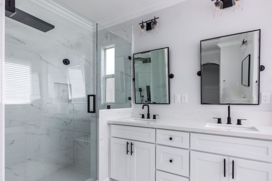 Bright white bathroom with double vanity, mirrors, glass shower, and black hardware
