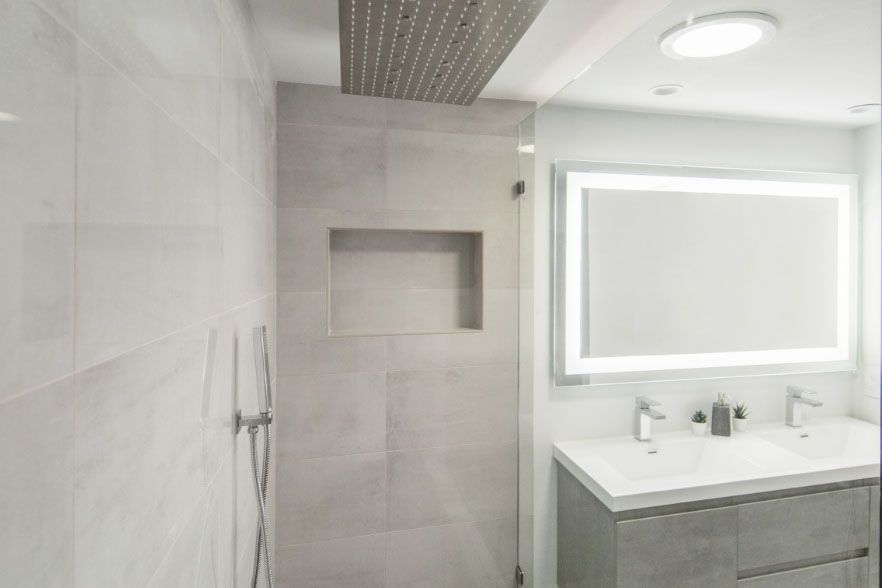 Modern white bathroom with tiled shower, recessed shelf, and vanity with large mirror.