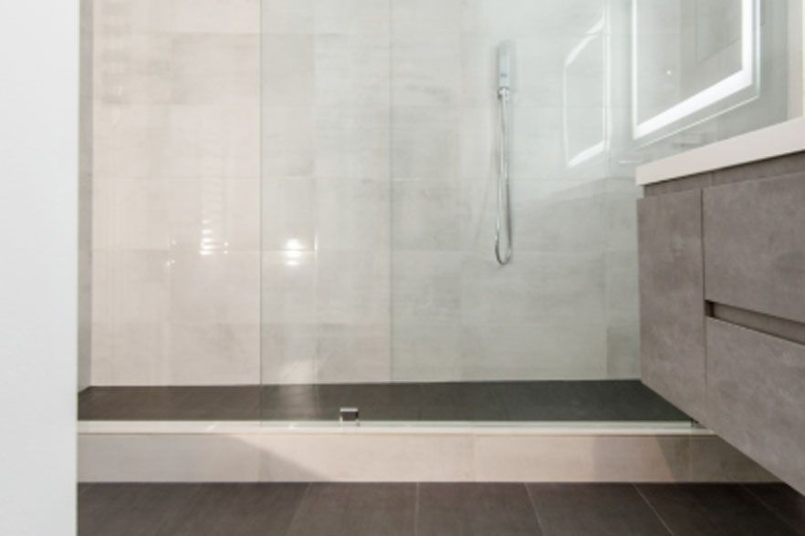 Modern bathroom with glass shower, gray tile, and a floating vanity beside the shower.