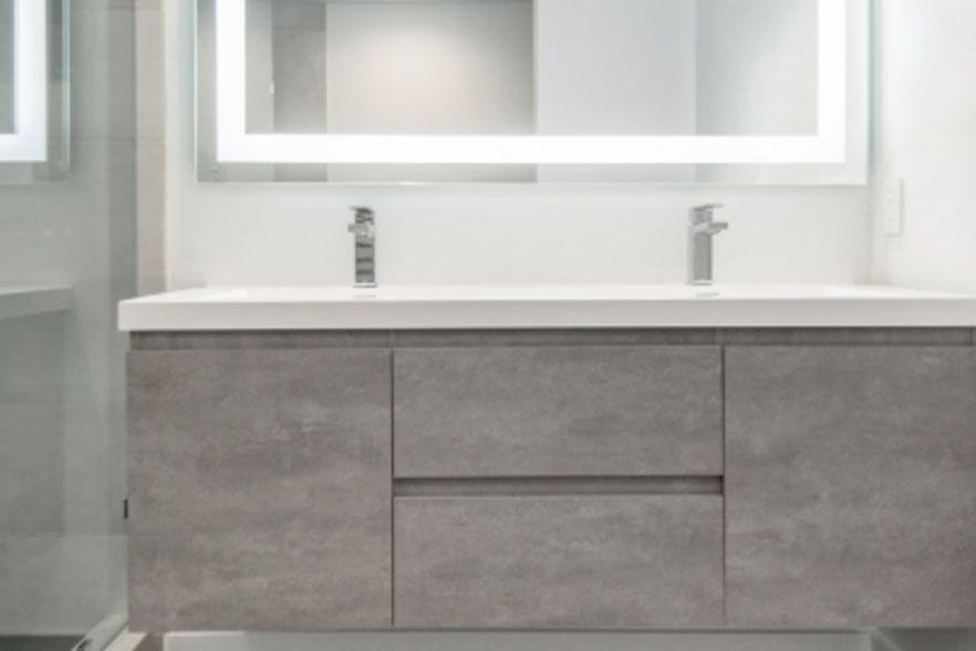 Modern bathroom vanity with gray drawers, white countertop, and illuminated mirror above the sink.