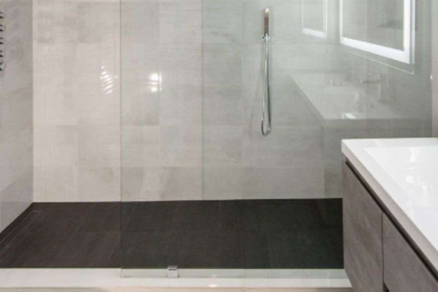 Modern tiled walk-in shower with glass partition, dark floor, and white vanity edge