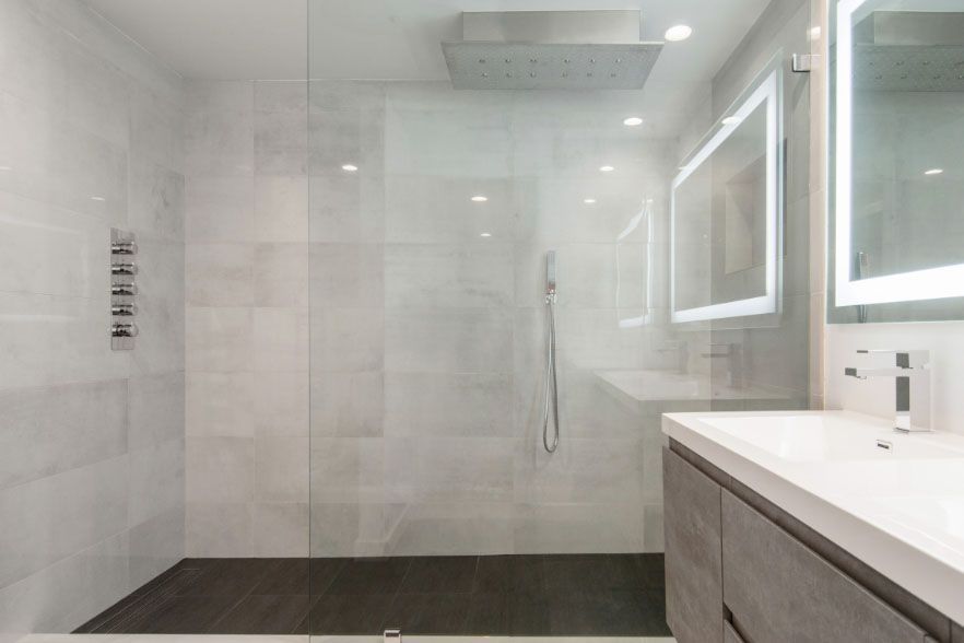 Modern bathroom with large walk-in shower, gray tile, and vanity with illuminated mirror.