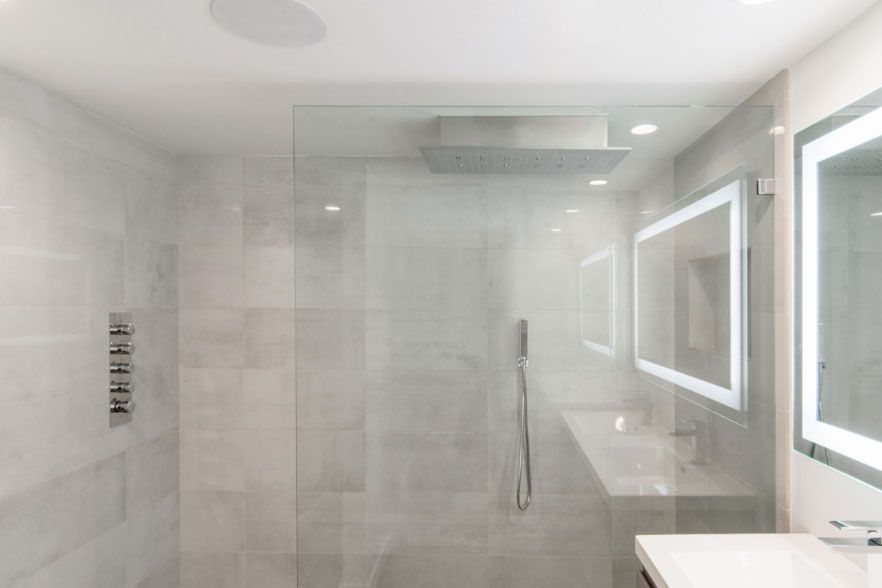 Modern white bathroom with glass shower, double vanity, and backlit mirrors