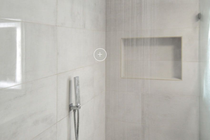 Modern tiled bathroom shower with handheld showerhead and recessed shelf niches.