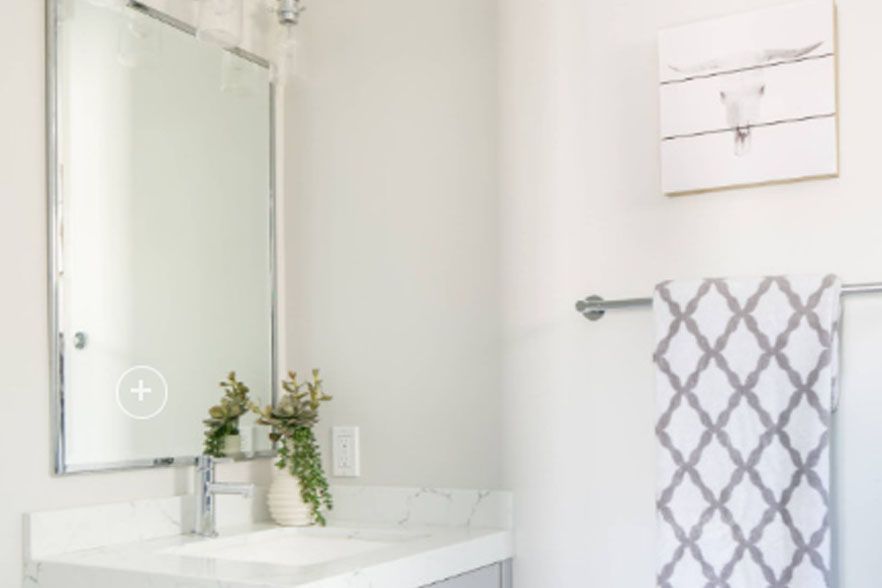 Bright bathroom vanity with mirror, white countertop, towel rack, and gray patterned hand towel
