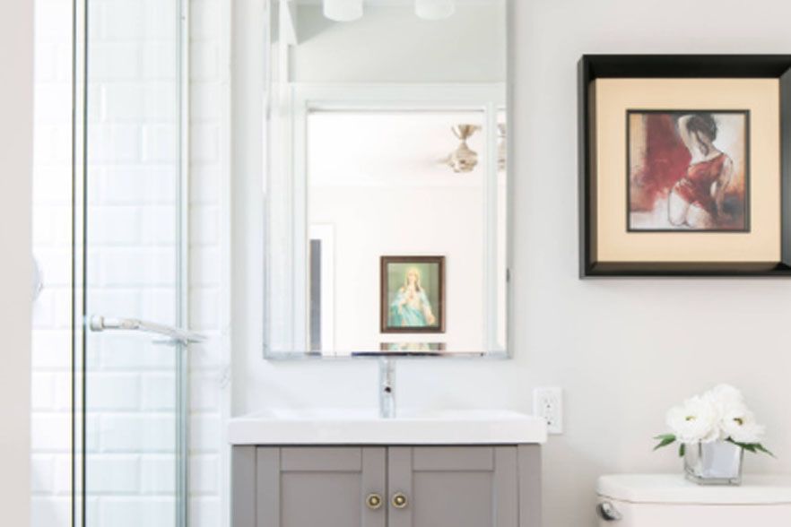 Bright bathroom with a white vanity, mirror, shower, and framed art on the wall.