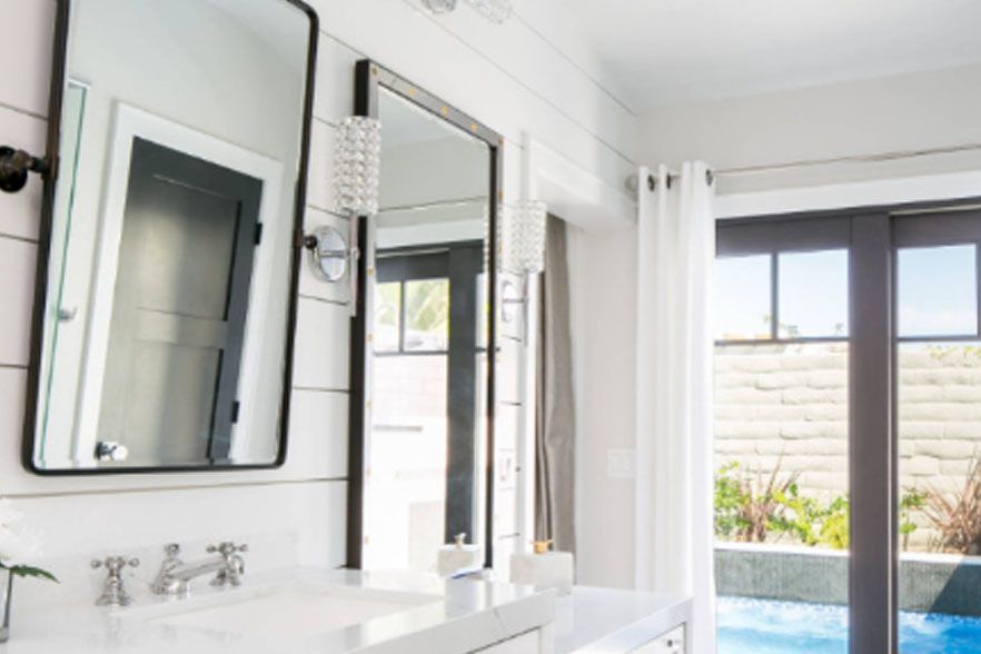 Bright bathroom vanity with mirrors beside a sliding glass door to a pool outside
