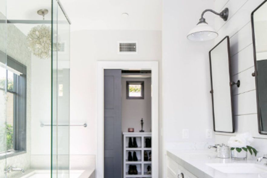 Modern white bathroom with glass shower, vanity, and built-in shelving behind a doorway