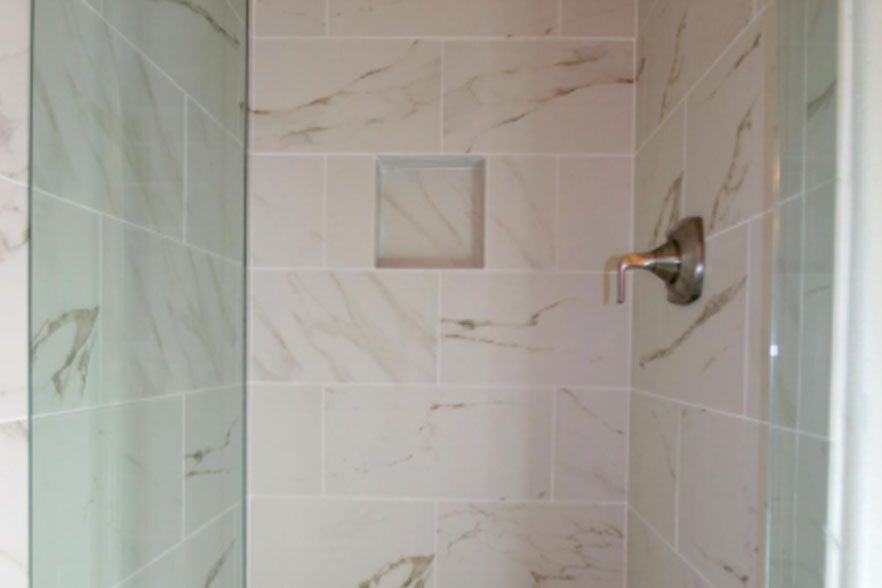 Empty tiled shower stall with glass doors and a chrome shower control handle