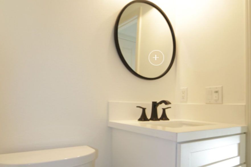 Small bathroom vanity with round mirror, black faucet, and white countertop beside a toilet.