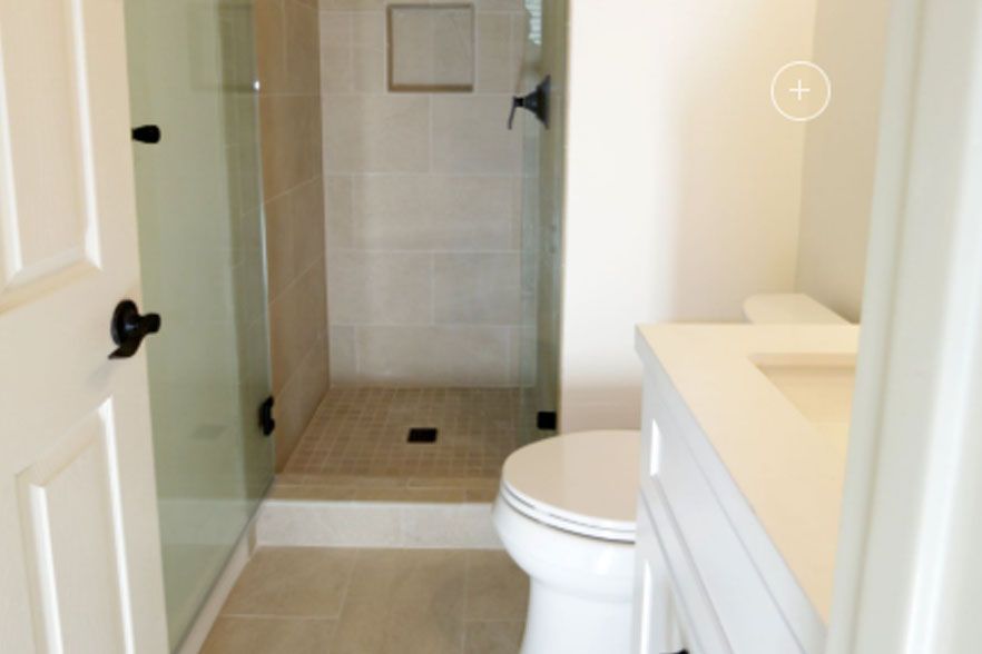 Small bathroom with toilet, glass shower, beige tile, and white vanity.