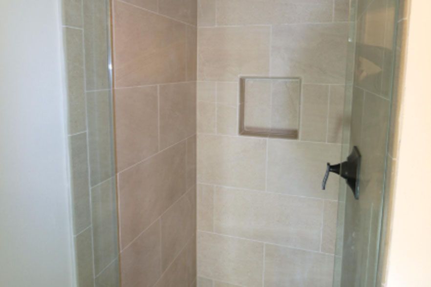 Tiled shower stall with a built-in niche and black shower handle, viewed through glass door