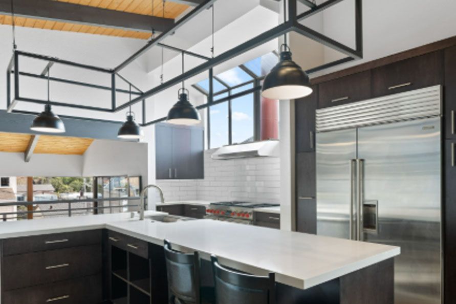 Modern kitchen with white island, dark cabinets, stainless fridge, and hanging pendant lights