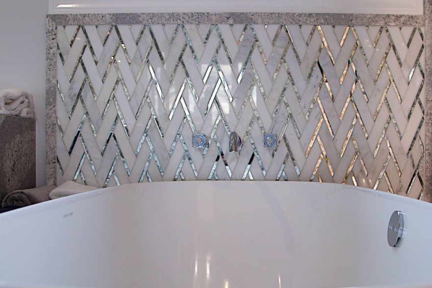 White bathtub in front of a mirrored chevron tile wall in a bathroom