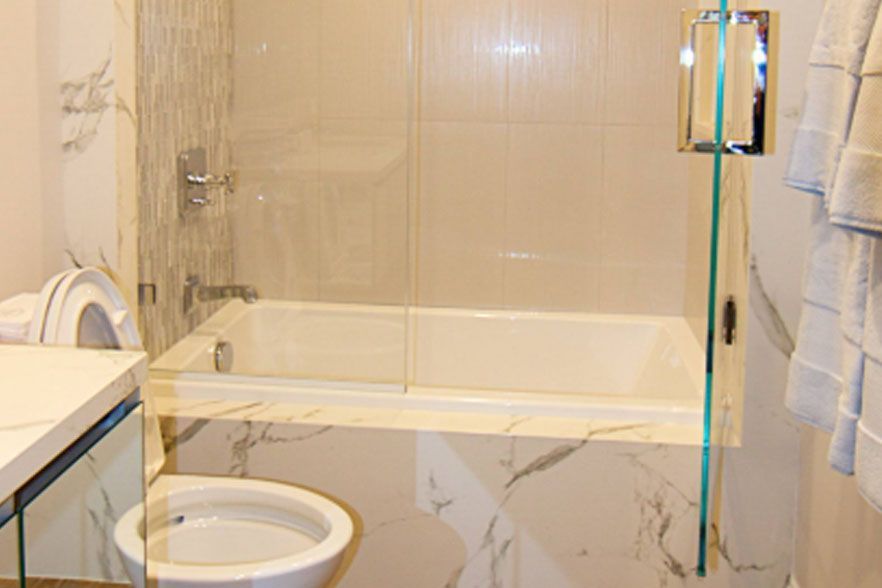 Bathroom with a glass shower enclosure, bathtub, toilet, and white towels on a beige tiled wall.