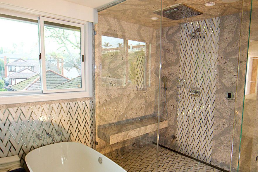 Marble-tiled bathroom with a tub, shower area, and window letting in daylight.