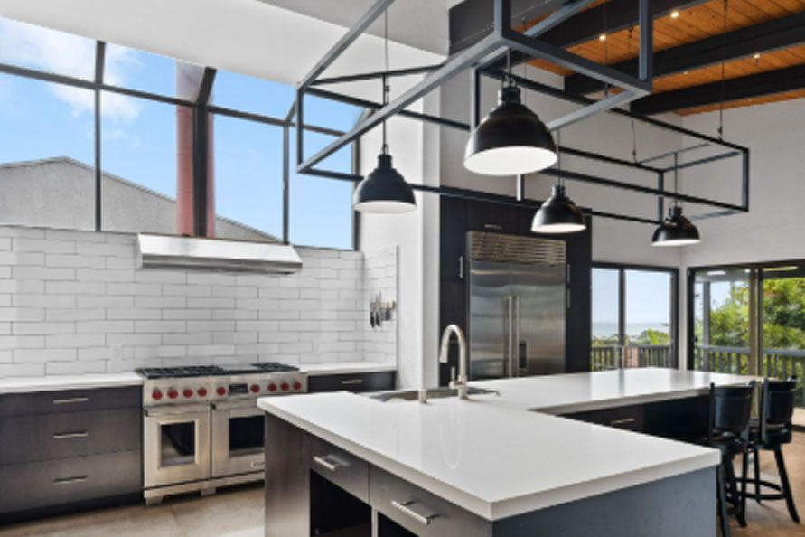 Modern kitchen with large island, black pendant lights, white tile backsplash, and floor-to-ceiling windows