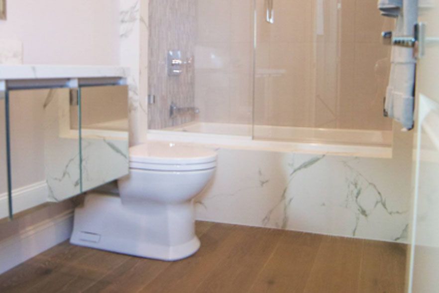 Modern bathroom with toilet, glass shower, marble accents, and wood-look flooring