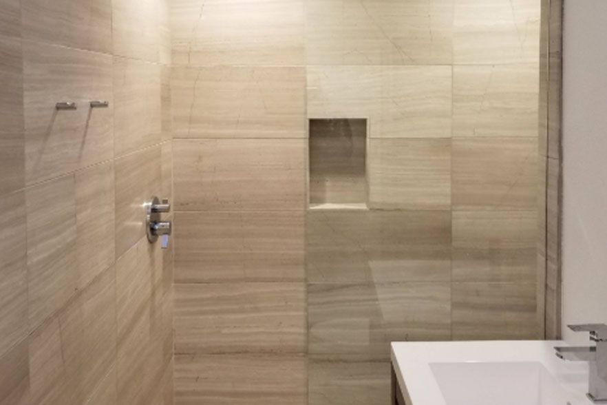 Modern beige tiled shower with built-in niche and white sink edge visible