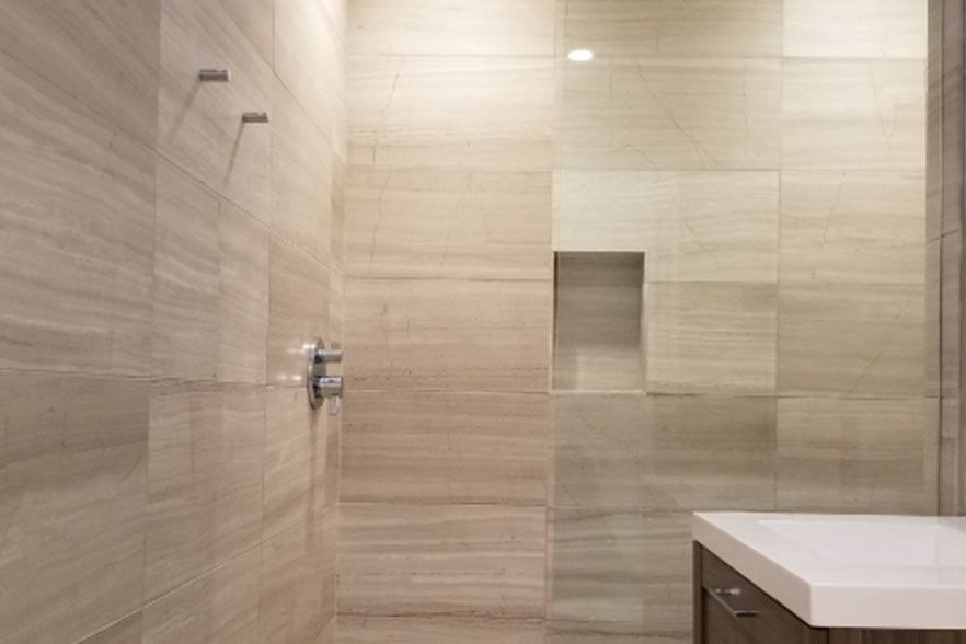 Modern beige-tiled bathroom with a walk-in shower and white vanity counter