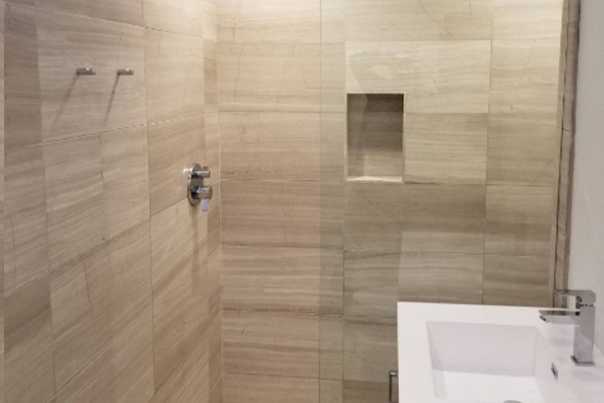 Beige tiled bathroom wall with shower controls, recessed niche, and white sink edge on the right