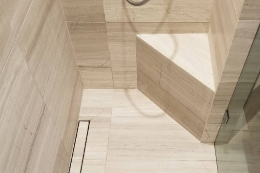 Small beige tiled shower with a glass panel and raised triangular seat or shelf area