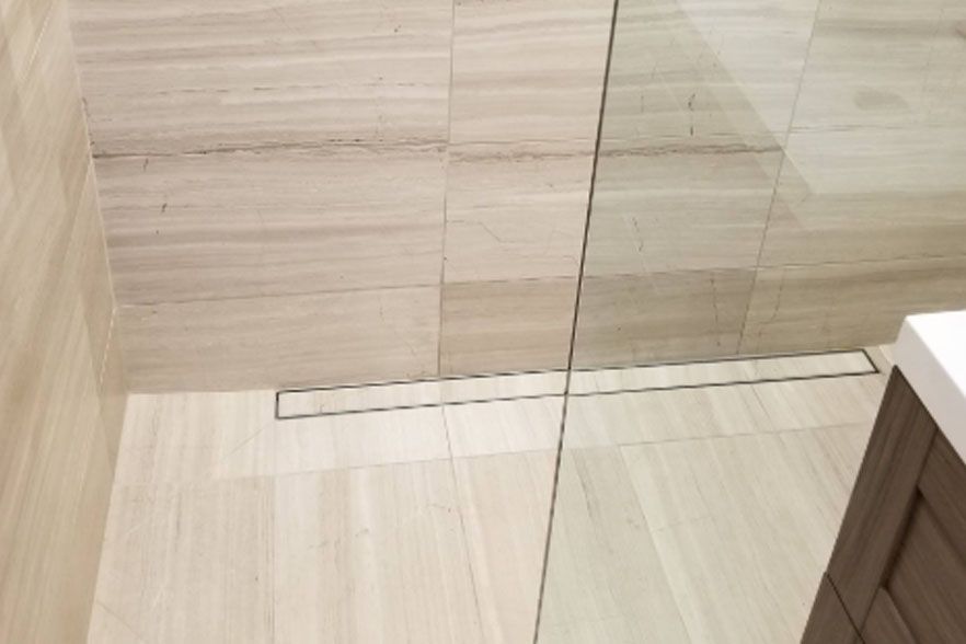 Modern bathroom shower area with beige tile walls, a glass partition, and a floor drain