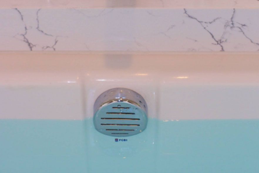 Bathtub drain cover with chrome vent, above light blue water and white marble tile trim