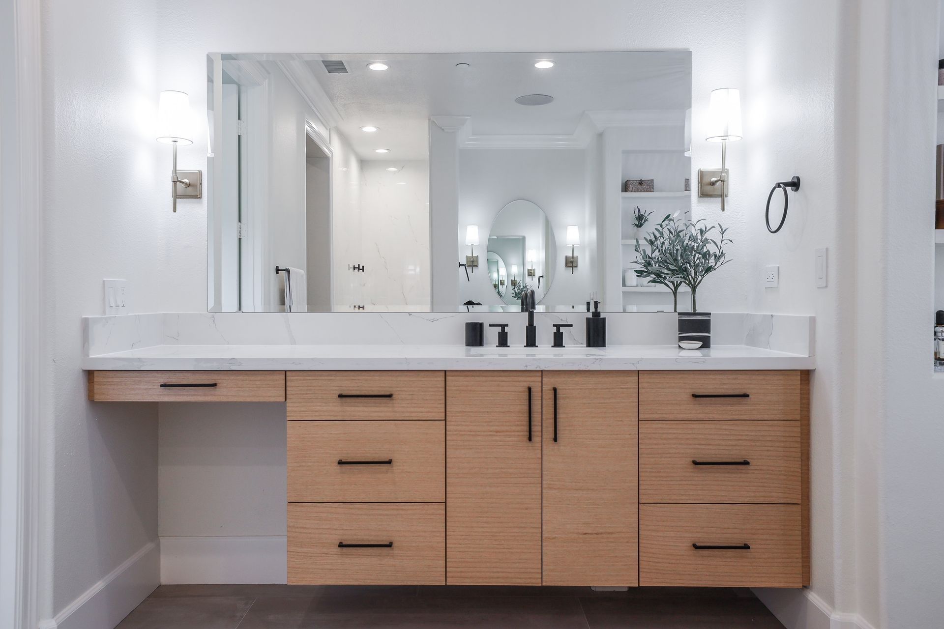A floating bathroom vanity with light wood cabinets, black hardware, a marble countertop, and a large wall-mounted mirror.