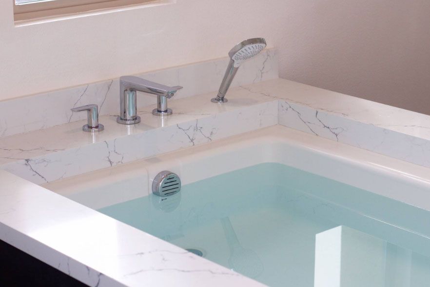White marble bathroom with a built-in bathtub, chrome faucet, and handheld showerhead filled with water