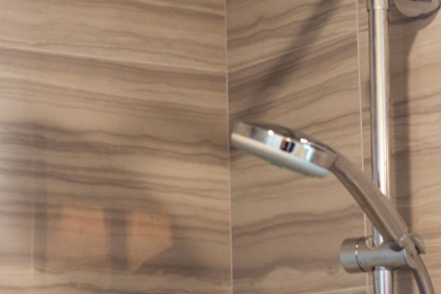 Close-up of a chrome showerhead against tan wood-patterned bathroom wall tiles.