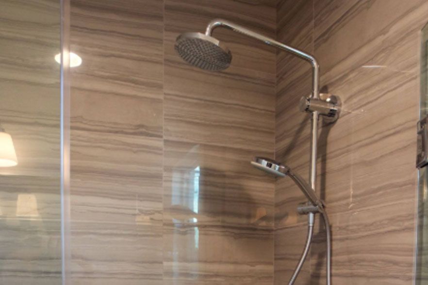 Modern shower with wood-pattern wall tiles, glass panel, and chrome rainfall and handheld showerheads