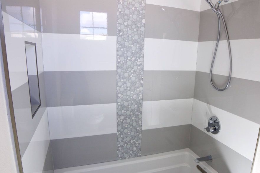 Modern bathroom with gray striped tile, a mosaic accent strip, bathtub, and handheld showerhead