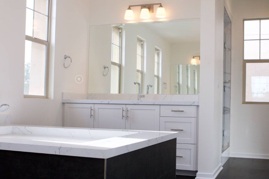 Modern bathroom vanity with large mirror, white cabinets, and dark countertop near a window.