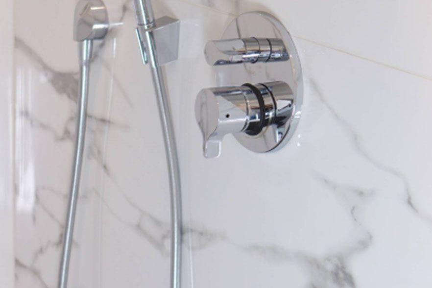 Chrome shower faucet and handheld showerhead against white marble tile wall