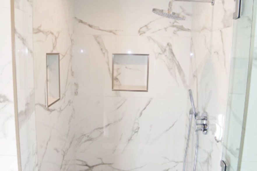 Marble-tiled shower with recessed niche, chrome fixtures, and glass door